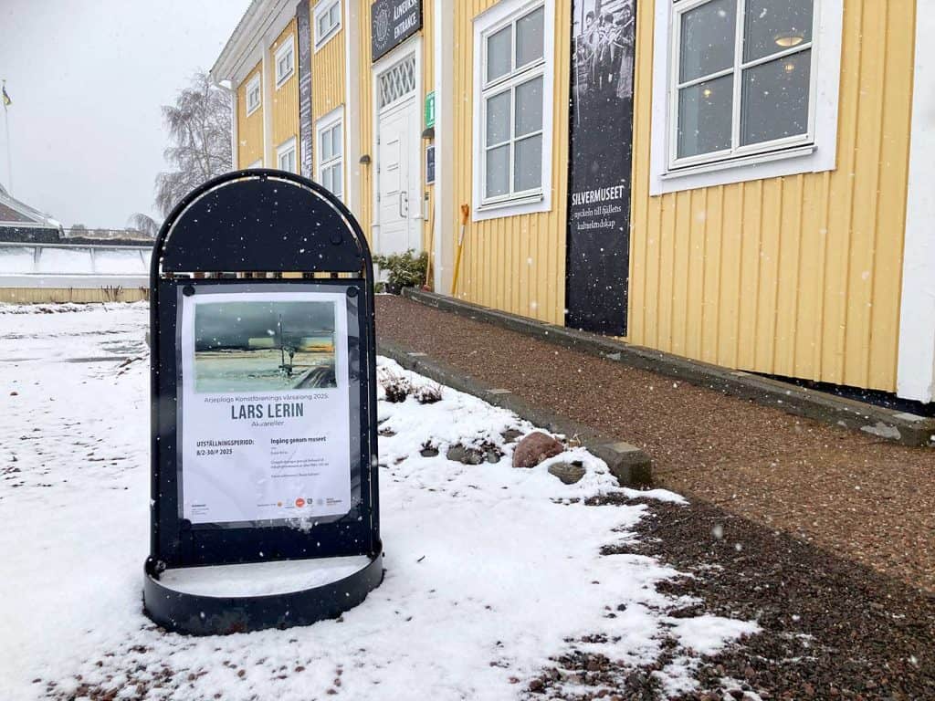 En skylt utanför entrén till Silvermuseet berättar att här visas en Lars Lerin utställning. Det är snö på marken runt skylten.