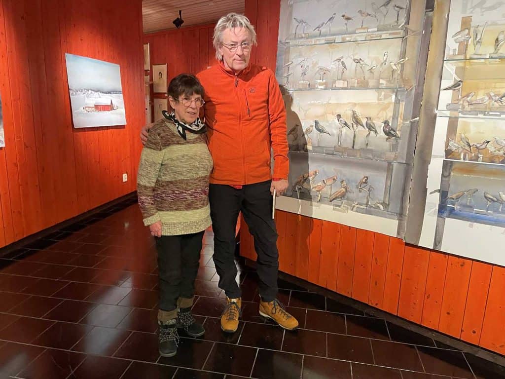 Barbro Holmström och Lars Lerin står vid varandra, tätt intill en stor målning med fågelmotiv. Bilden är tagen vid vernissage för Lerins utställning.