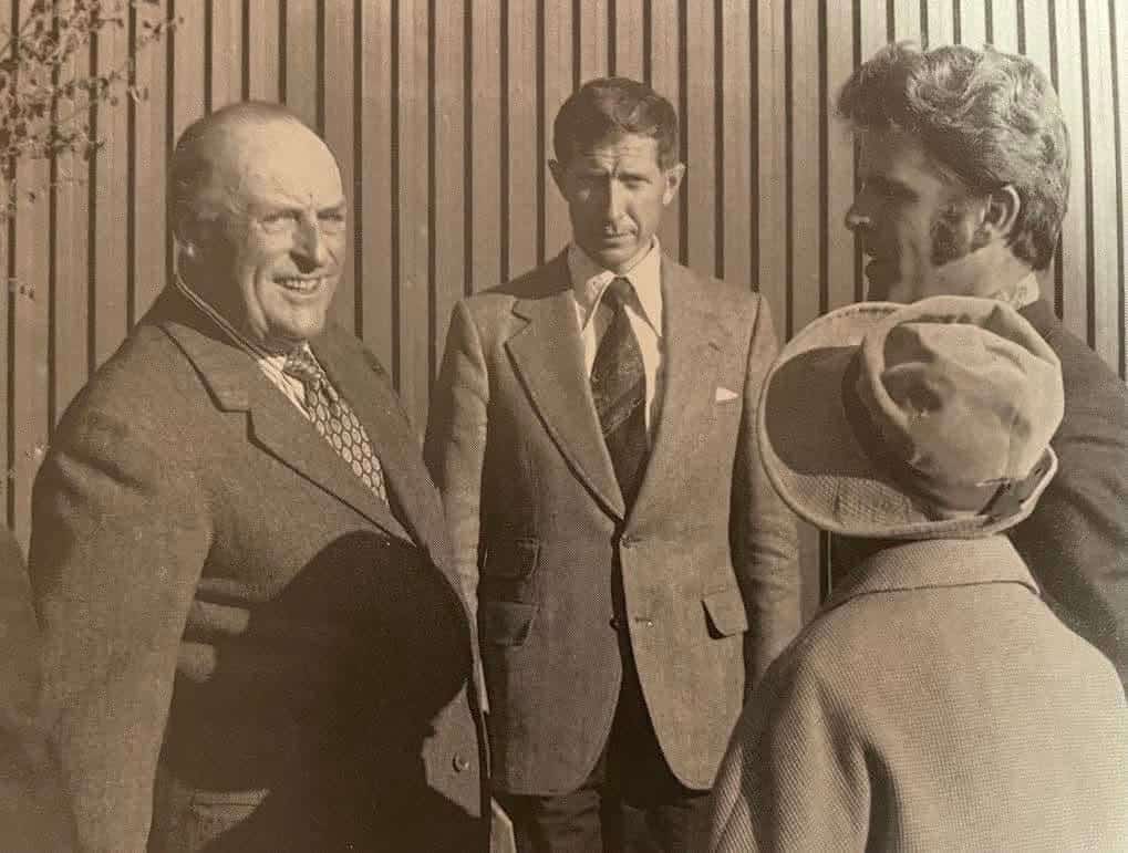 Gammal bild. Tre kostymklädda män, och ryggen av en kvinna i hatt syns. De pratar med varandra.