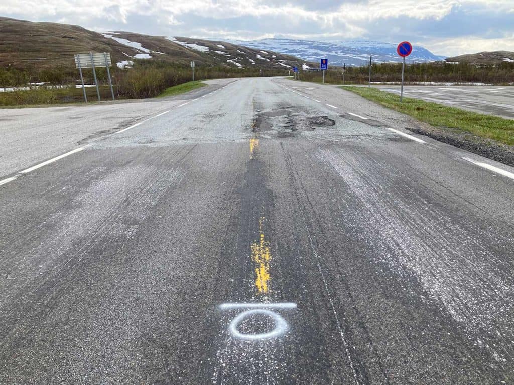 En bild av asfalterad väg. I förgrunden syns vita markeringar mitt på vägen. Dom övergår sedan till gula markeringar.