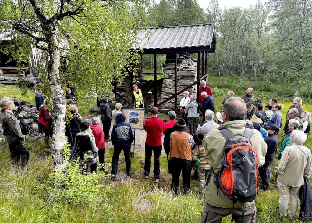 Människor med ryggen mot kameran, vända mot en stor stenugn. Vid stenugnen står en kvinna i varseljacka, som pekar och berättar om ugnen.