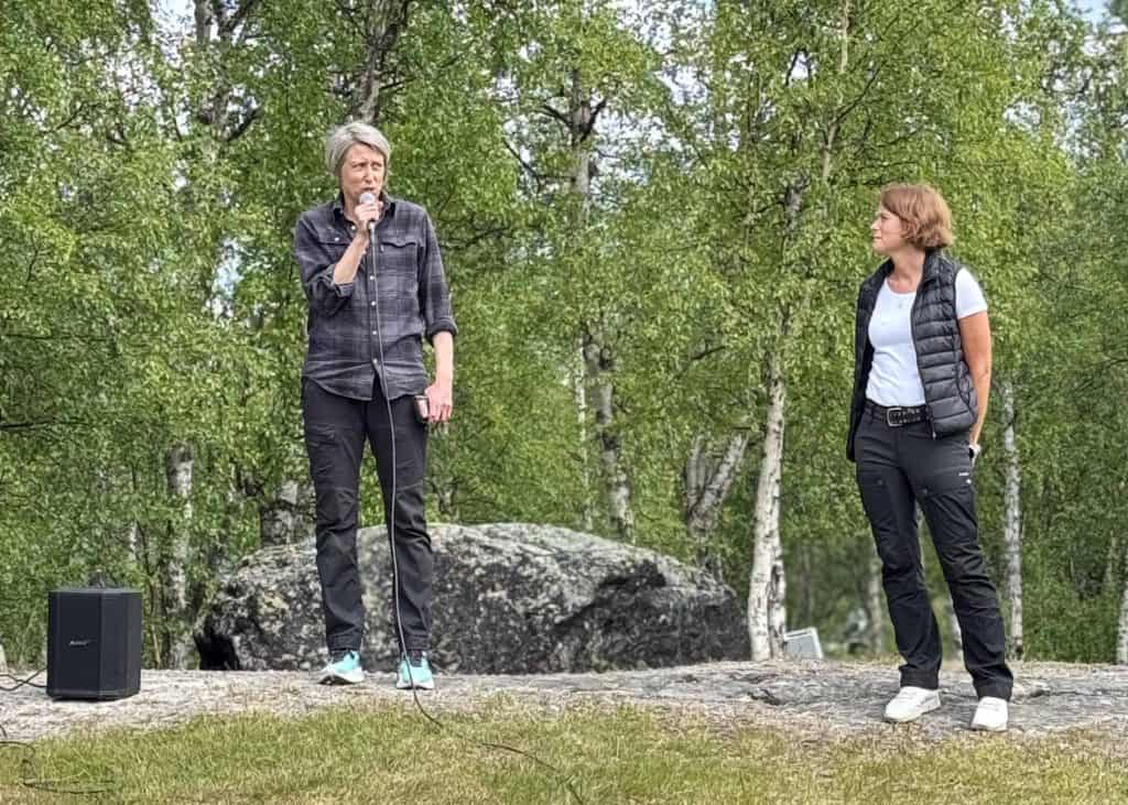 Två kvinnor i sommarmiljö, med gröna björkar bakom sig. Den ena kvinnan håller i en mikrofon.