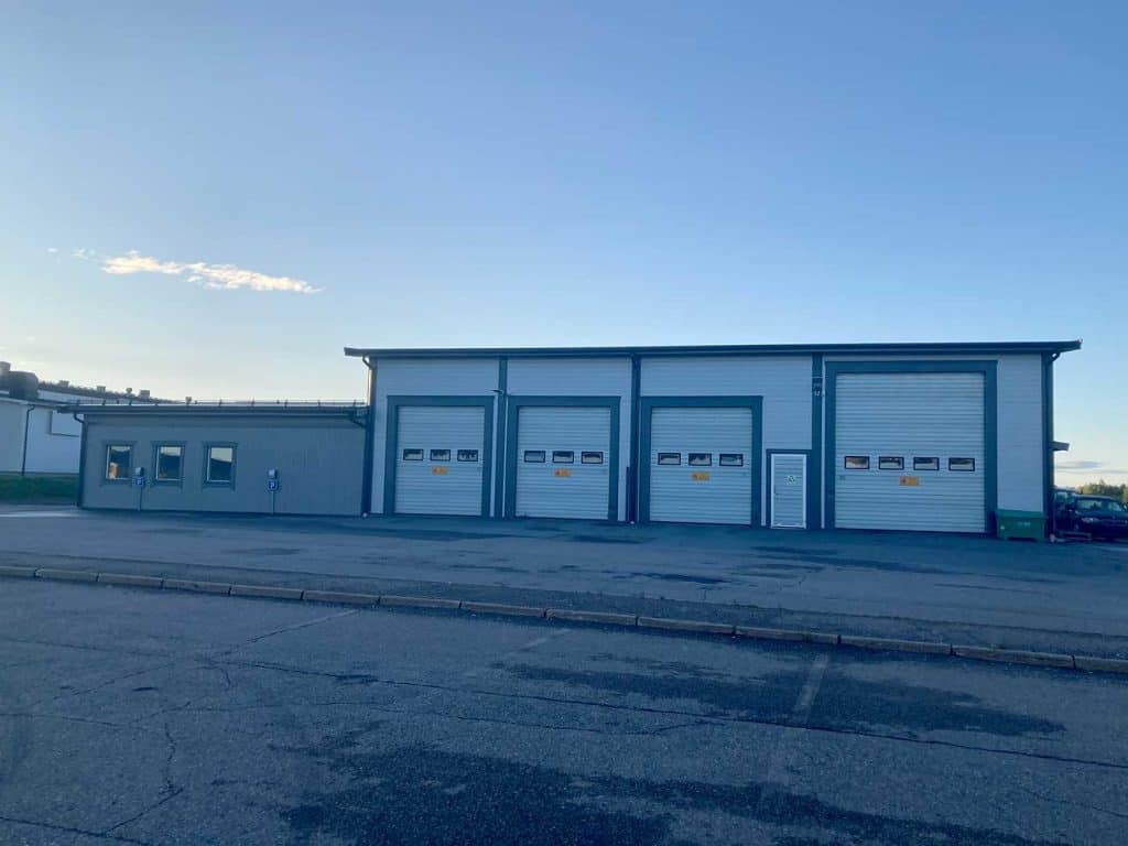 En byggnad med tre garageportar för vanliga bilar och en större. Ytan framför byggnaden är asfalterad. 