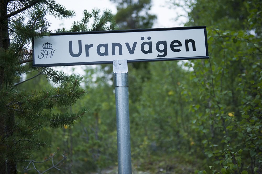 Fokus på en vägskylt med texten Uranvägen. Bredvid och bakom skylten syns tall och björk.
