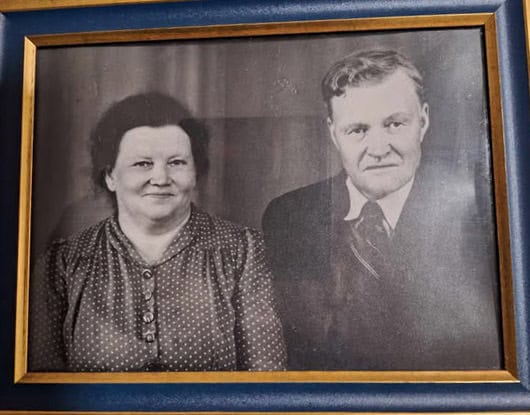 Gammal inramad svartvit bild av en kvinna och en man. De är finklädda och ler lite mot fotografen.