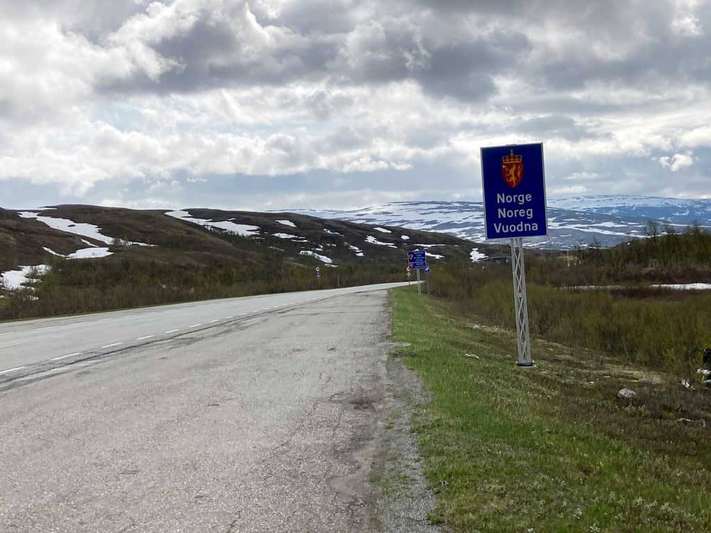 Bild på en asfalterad väg. Vid sidan av vägen står en skylt med texten Norge Noreg Vuodna.
