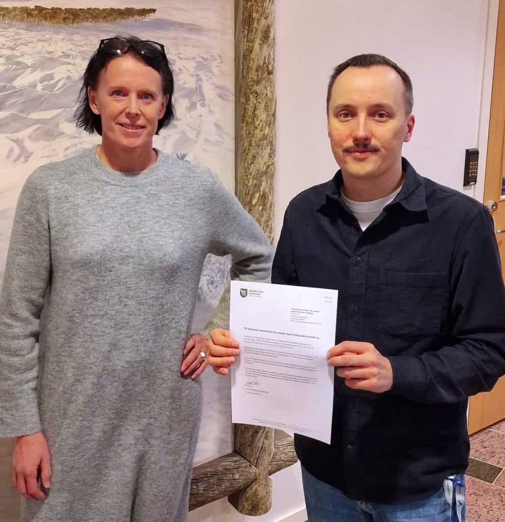 En kvinna och en man står bredvid varandra. De ler, men ser också bestämma ut. Mannen håller upp ett papper framför sig. 