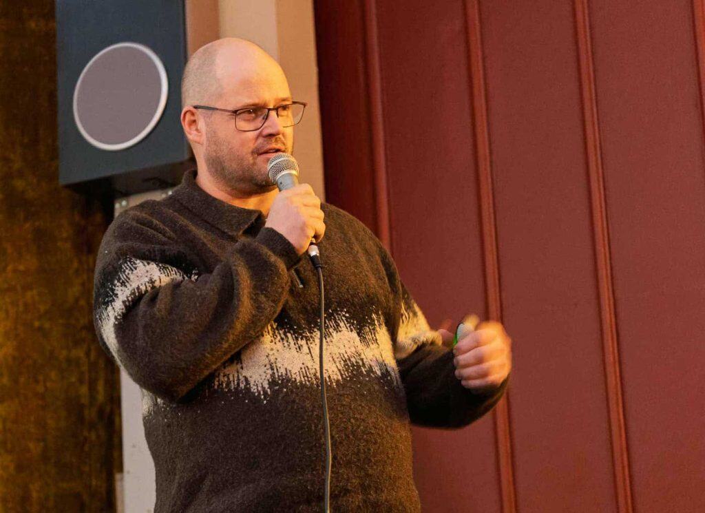 Bild på en man med mikrofon i handen. Han pratar och gestikulerar.