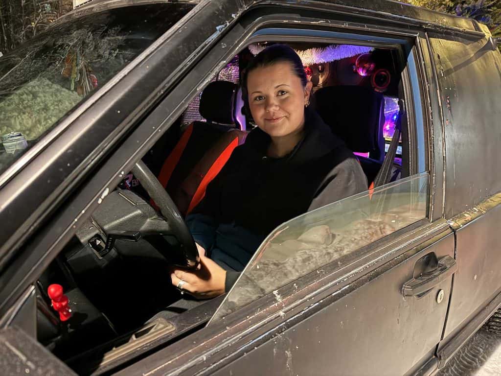 En närbild på en tjej som sitter bakom ratten i sin EPA, med öppen sidoruta. Hon ser glad ut.